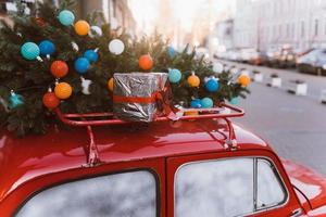 Red retro car with a Christmas tree fir tied to the roof. photo