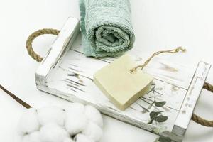 un jabón de fregar blanco, una rama de eucalipto y una toalla de algodón para spa se encuentran en una bandeja de madera blanca. concepto positivo del cuerpo foto