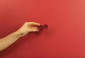 A womans hand holds a red heart on a red background photo