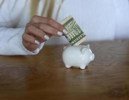 A woman puts a dollar banknote into a piggybank for saving purposes photo