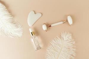 A white Guasha face massager and a face serum lying on a beige background photo