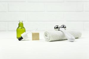 un aceite verde cbd, un rodillo facial, una toalla blanca de algodón yacen sobre una mesa blanca foto
