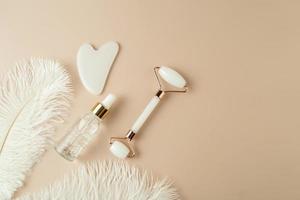 A white Guasha face massager and a face serum lying on a grey background photo