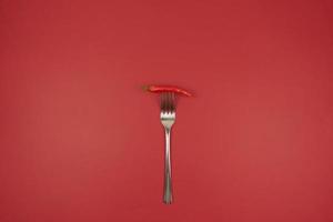 A red hot chili pepper on a fork on a red background photo