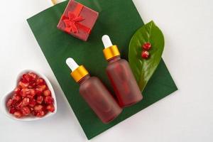A red dropper bottles of pomegranate serum or oil lying on a green paper shopping bag as a present for holidays photo