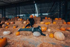 A guy and a girl with pumpkins on their heads are lying in the hay photo