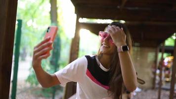 Young woman in pink sunglasses takes selfie photo with smart phone video