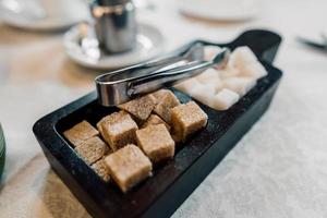 Bowl with pieces of white and brown sugar cubes and with sugar-tongs. photo