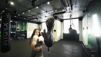 Young woman in a boxing gym punches double end bag with white boxing gloves