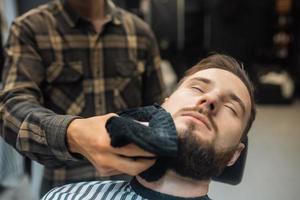 Barber preparing man face for shaving with hot towel in barber shop photo