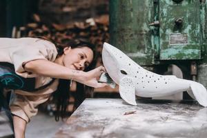 Portrait of young woman carefully work on a ceramic whale in workshop. photo