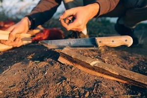 Man chops wood with a large bonfire knife on a sunny day. photo