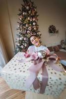 niña dando un regalo en el fondo de un árbol de navidad foto