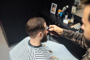 maestro en barbería hace corte de pelo de hombres con cortapelos foto