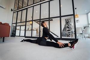 mujer joven con traje deportivo negro haciendo pose de yoga en el interior. foto