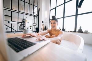 Young woman working on laptop while taking a bathtub photo