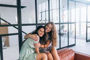 Happy girls embracing at home sitting on a couch in the living room photo