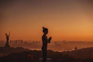 Woman doing yoga on the roof of a skyscraper in big city. photo