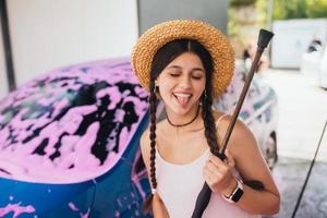 Woman with hose stands near car covered in pink foam photo