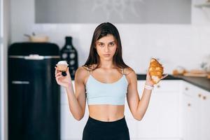 A young woman holds a croissant and a cake in her hands. photo