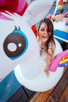 Happy young woman sitting on inflatable unicorn toy mattress photo