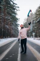 Skateboarder standing on the road in the middle of the forest, surrounded by snow photo