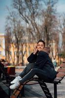 young woman sitting on bench in park, smiling and looking into the camera photo