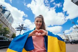 mujer joven con bandera ucraniana muestra el corazón con las manos foto