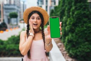 mujer que muestra un teléfono inteligente moderno con pantalla verde para reemplazo foto