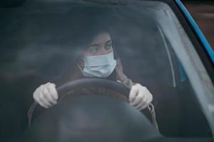 Young woman in a mask and gloves driving a car. photo