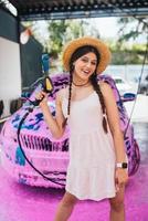 Young woman hose stands in front of a car covered in pink foam photo