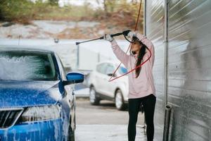 Young woman washing blue car at car wash photo