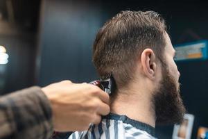 Master in barbershop makes men's haircutting with hair clipper photo