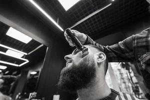 Barber works with a beard clipper. Hipster client getting haircut. photo