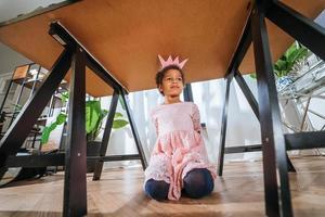 Little girl is playing under the table tongue in the camera photo