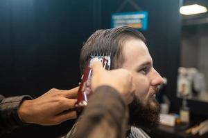 Master in barbershop makes men's haircutting with hair clipper photo