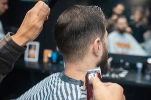 maestro en barbería hace corte de pelo de hombres con cortapelos foto