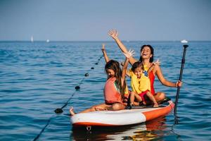 Mother with two daughters stand up on a paddle board photo