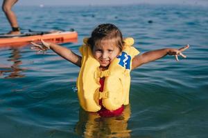 niña pequeña en un chaleco salvavidas bañándose en el mar. foto