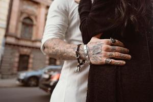 The man's hand in tattoos and jewelry embraces a girl's waist. photo