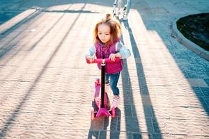 Little girl with blonde hair rides on scooter photo