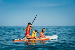 Mother with two daughters stand up on a paddle board photo