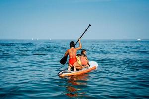 Mother with two daughters stand up on a paddle board photo