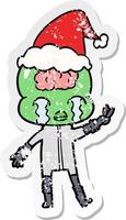 distressed sticker cartoon of a big brain alien crying and giving peace sign wearing santa hat vector