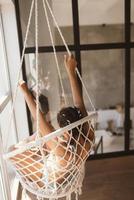 Young woman in underwear at hanging chair at room. photo