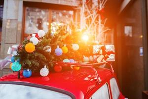 Red retro car with a Christmas tree fir tied to the roof. photo