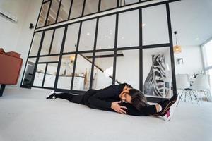 Young female wearing black sports suit exercising yoga pose indoors. photo