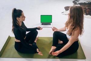 Two young women meditating in lotus pose at home photo