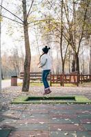 Happy school girl jumping on a small trampoline in the park photo