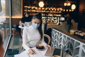 Pretty woman wearing medical face mask, using laptop to work. photo